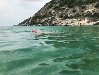 People swimming in sea against rocks