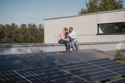 Man and woman with daughter sitting on wall by solar panel