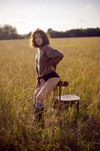  portrait woman in a sweater and shorts sitting on a field with grass on a wood chair in autumn
