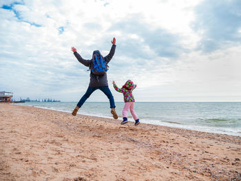 Full length of friends enjoying at beach against sky