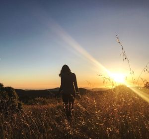 Rear view of silhouette woman on field against sky during sunset