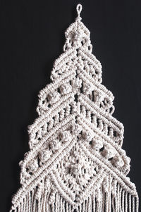 Christmas tree ornament macrame from white natural cotton threads on a black background. 