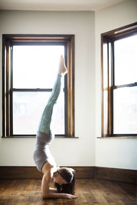 Woman performing handstand against window at home