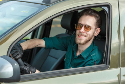 Portrait of a young man in dark glasses driving a car and smiling