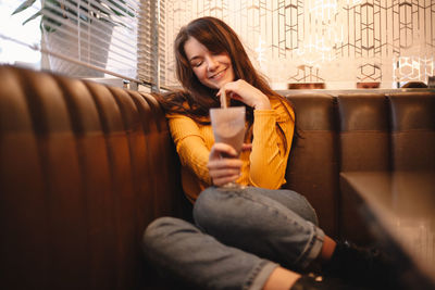 Happy teenage girl holding chocolate milkshake while sitting in cafe