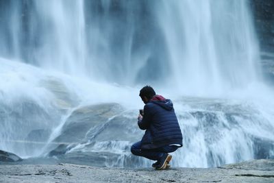 Rear view of man photographing waterfall