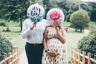 Couple holding balloon standing at park