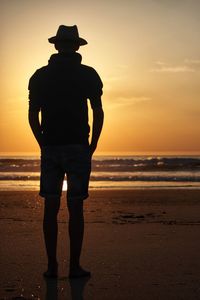 Silhouette man standing on beach against sky during sunset