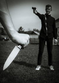 Cropped hand holding knife against man with gun