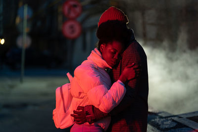 Affectionate sad young couple hug at dark street saying good bye to each other. farewell concept