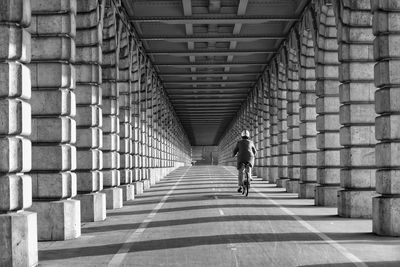 Rear view of person riding bicycle on road amidst colonnades