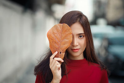 Portrait of young woman holding leaf outdoors