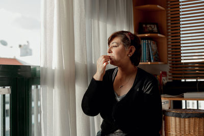 Young woman looking through window at home