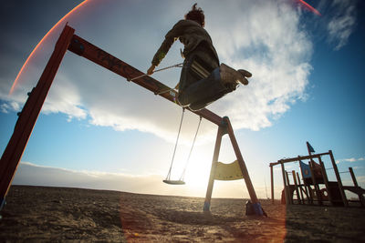 Low angle view of woman swinging at playground against sky during sunset