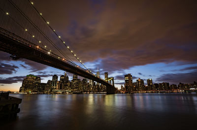 Illuminated bridge over river against sky in city at night