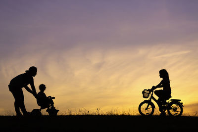 Silhouette people riding bicycles on field against sky during sunset