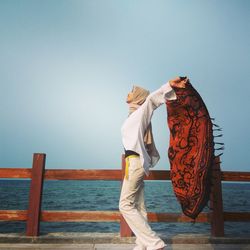 Side view of woman holding scarf at promenade against sky
