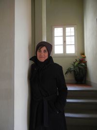 Portrait of young woman standing against window