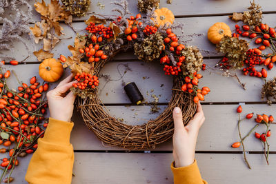 Girl making floral autumn door wreath using colorful rosehip berries, rowan, dry flowers and pumpkin