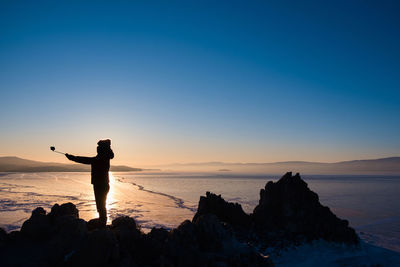 Silhouette man standing on rock at beach against sky during sunset