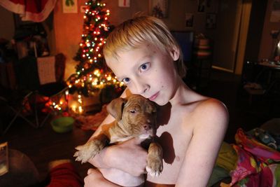 Shirtless boy holding dog during christmas dog at home