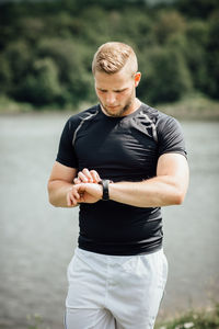 Young man checking time against lake