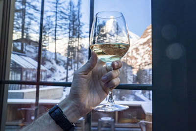 Man holding wineglass against matterhorn seen through glass window at resort