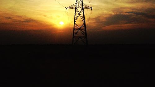 Low angle view of electricity pylon at sunset