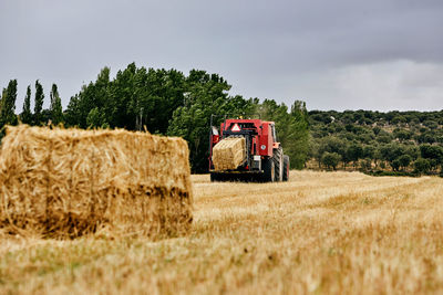 Dried hay roll and modern tractor placed on agricultural field in mountainous area in summer