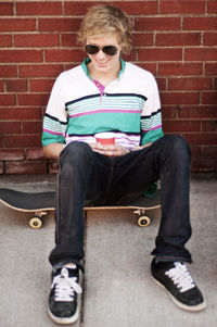 High angle view of man holding coffee cup while sitting on skateboard against brick wall