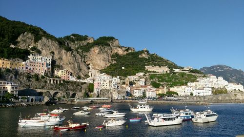 Boats moored on sea by cityscape against clear sky