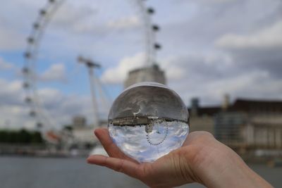 Close-up of hand holding crystal ball against sky