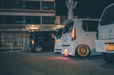 Cars parked on illuminated road by building at night