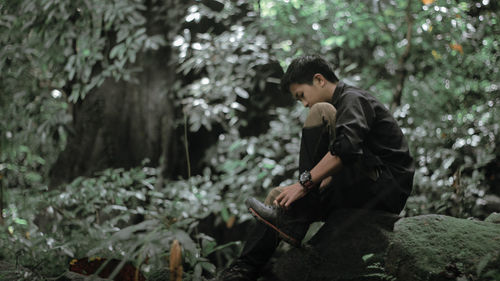 Side view of teenage boy holding plant in forest