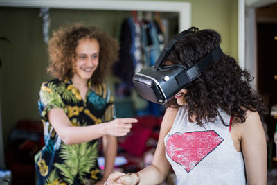 Smiling teenage boy pointing at girl wearing virtual reality headset at home