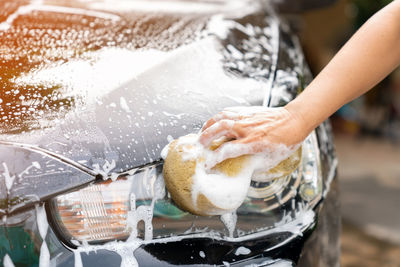 Woman use sponge washing black car head lights at home.