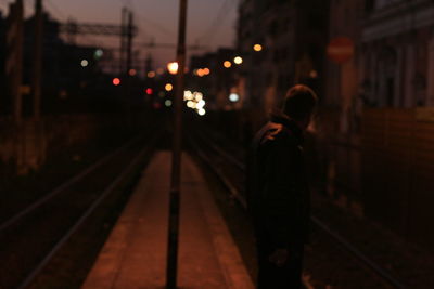 Rear view of person walking on illuminated railroad tracks at night