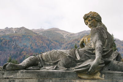 Close-up of old weathered female statue by mountains against sky