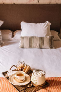 From above of tray with waffles with tea in cup and kettle placed on soft bed in morning