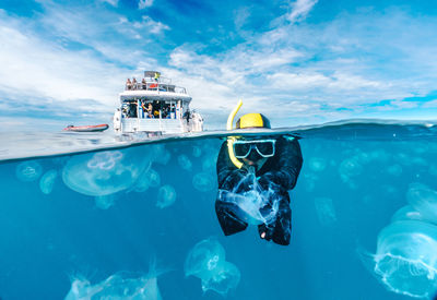 A woman in a black wetsuit is in the water with jellyfish. the jellyfish are floating around her