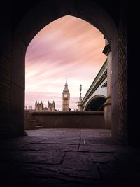 Big ben seen through arch against sky in city during sunset