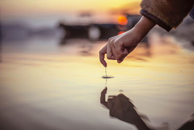 Midsection of person holding sea against sky during sunset