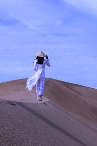 Woman on sand dune in desert against sky