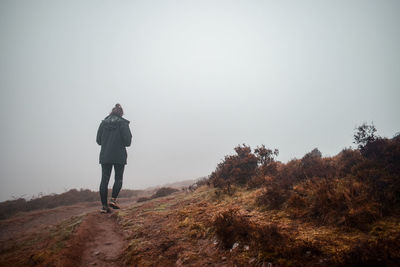 Rear view of female hiker walking on land against sky during winter