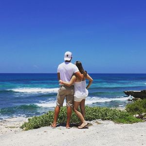 Rear view of couple standing on beach against clear sky