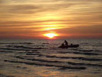 Silhouette people on sea against sky during sunset