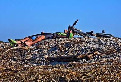 Low angle view of man lying down on land against clear blue sky