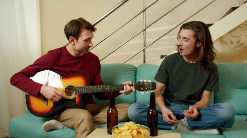 Homosexual couple playing guitar at home