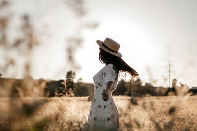 A girl in a wheat field wearing a dress and a straw hat. the girl is circling in the field.