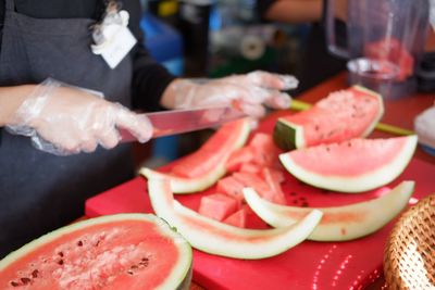 Midsection of woman cutting watermelon in shop